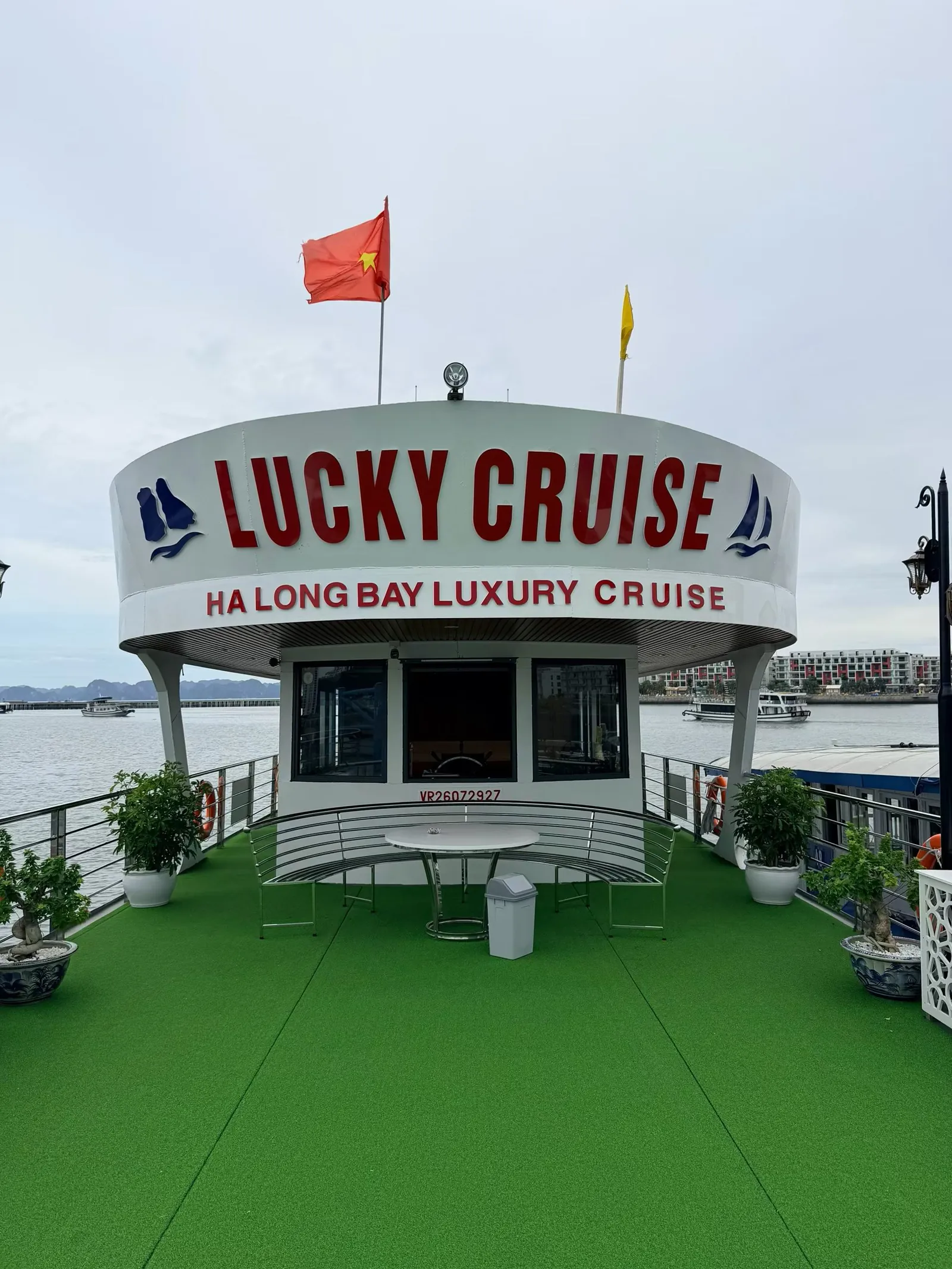 下龙湾游船甲板，绿色人工草坪上方是写着 LUCKY CRUISE 的船舱，旗杆上飘着越南国旗